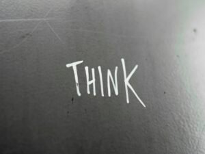 Weiße Wand mit großem schwarzen Schriftzug 'think', aufgenommen von Rob Coates. Klare Linien und minimalistisches Design.