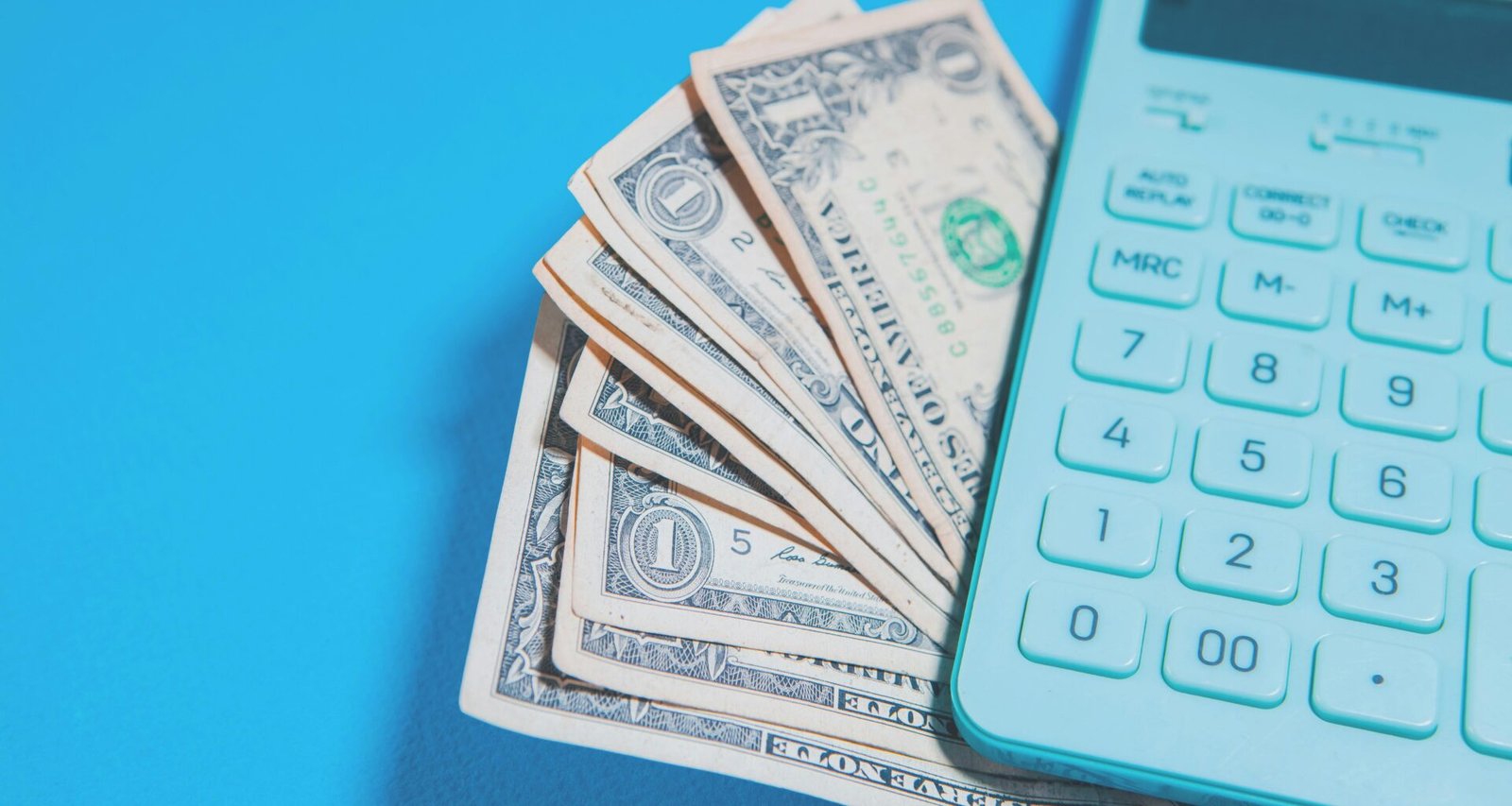US-Dollar Geldscheine und ein Taschenrechner auf blauem Hintergrund als Symbol für Finanzen und Kalkulation