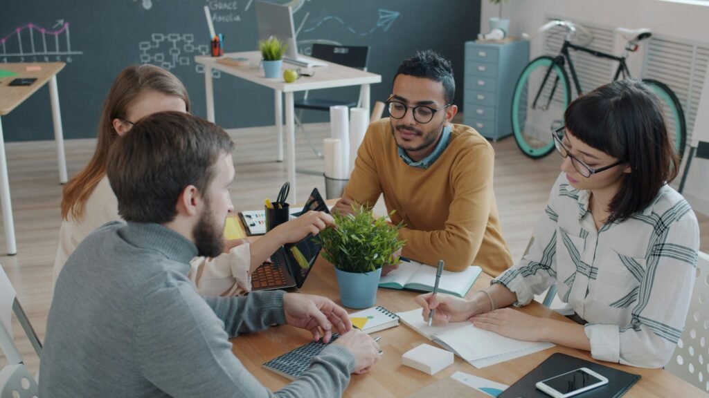 Ein vielseitiges Team sitzt in einem modernen Büro um einen Tisch und arbeitet konzentriert an einem Projekt.