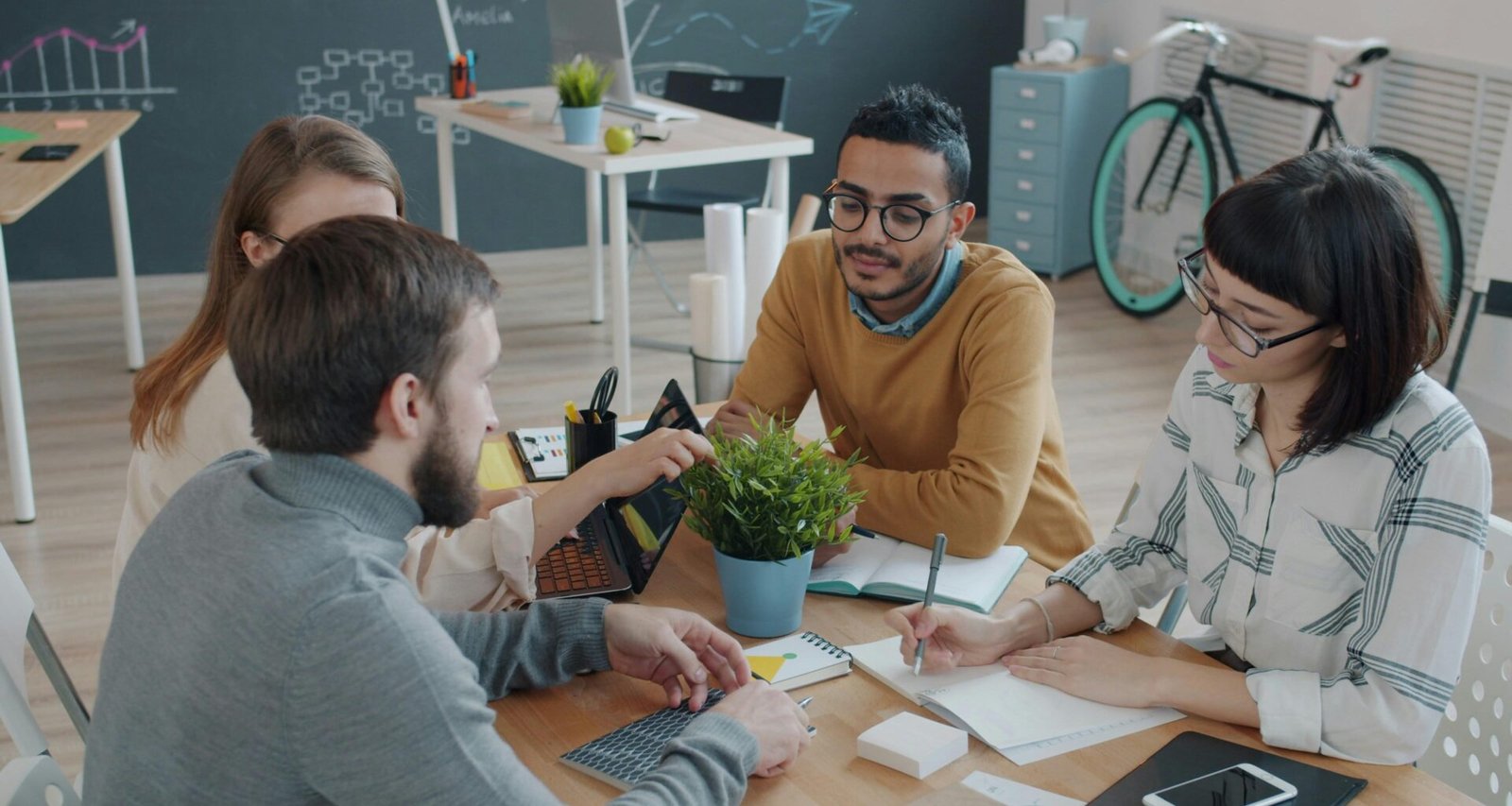Gruppe von Mitarbeitern unterschiedlicher Herkunft bespricht Projektideen an einem Tisch in einem modernen Büro.