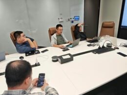 Vier Männer sitzen mit Laptops an einem Konferenztisch in einem modernen Besprechungsraum und diskutieren gemeinsam.
