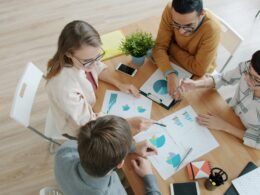 Vier Personen besprechen gemeinsam an einem Tisch Diagramme und Charts im Rahmen einer Teamkollaboration.
