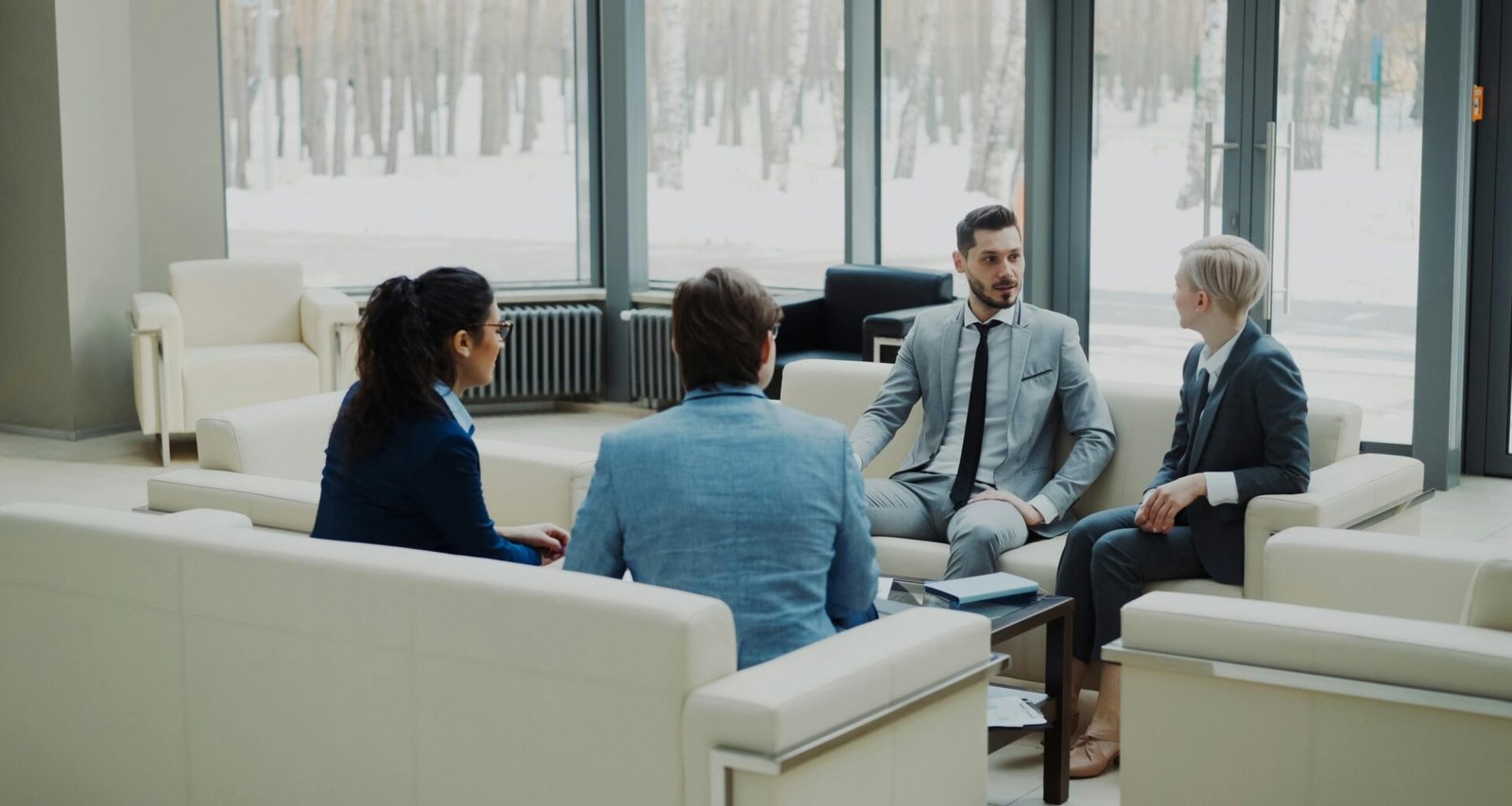 Vier berufstätige Personen sitzen in einem modernen, lichtdurchfluteten Konferenzraum bei einem Meeting.