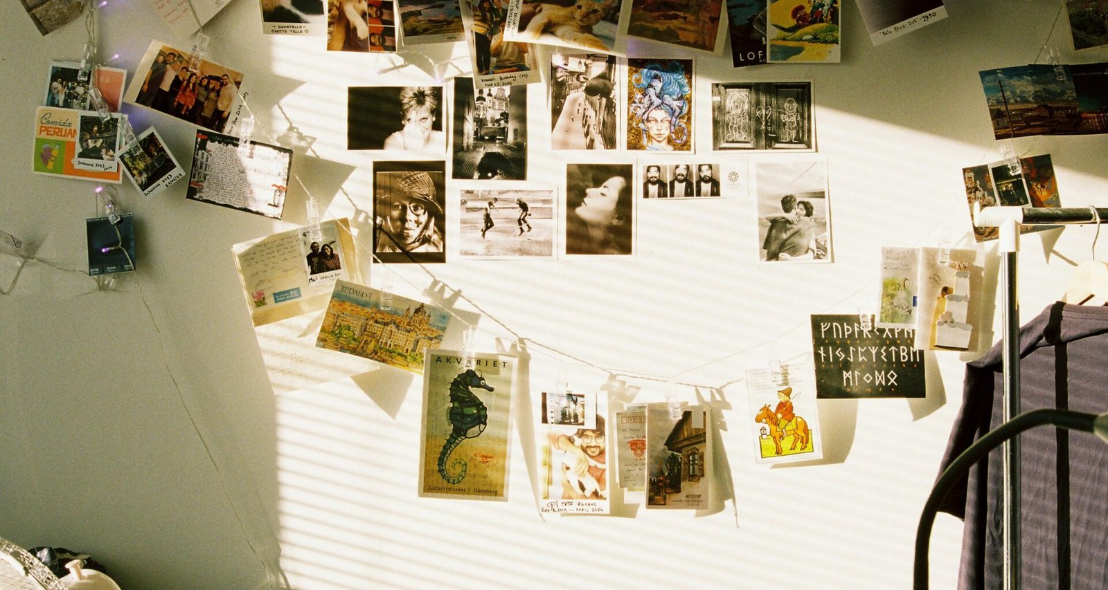 Wand mit Postkarten, aufgehängt an Schnüren und illuminiert durch Lichterketten, als kreative Raumdekoration