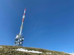 Weiß-roter Turm am Rand eines grünen Feldes, aufgenommen bei Tageslicht, neben einer kleinen Wiese, mit klarem Himmel