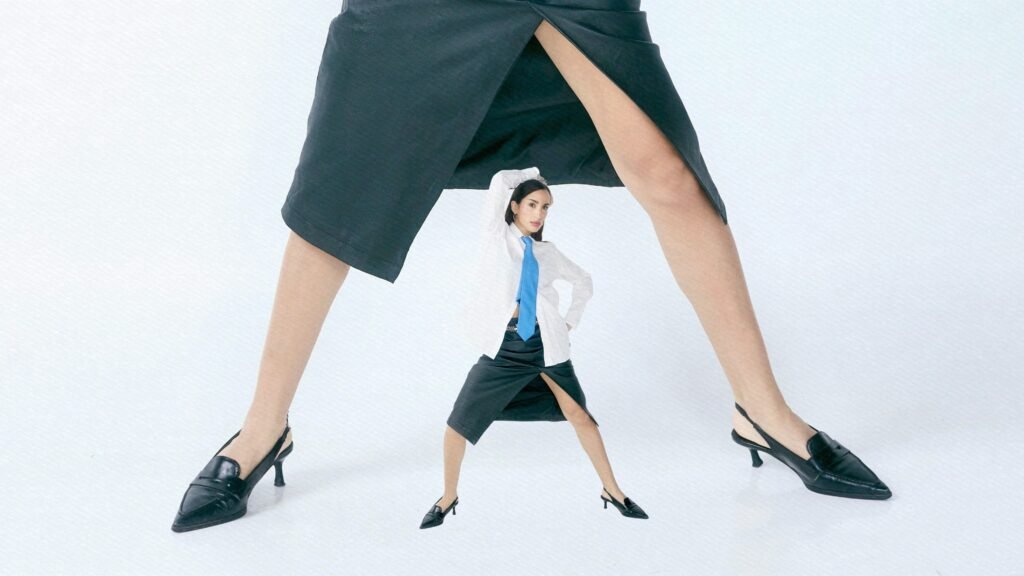 Eine winzige Frau steht zwischen zwei riesigen Beinen in langen Röcken und verdeutlicht deutliche Größenkontraste.