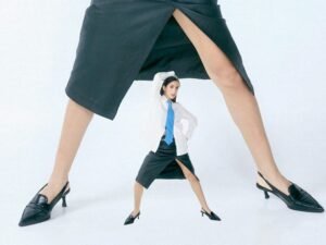 Eine winzige Frau steht zwischen zwei riesigen Beinen in langen Röcken und verdeutlicht deutliche Größenkontraste.