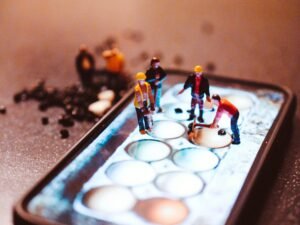 Mehrere Miniatur-Bauarbeiter sind auf dem Bildschirm eines Handys bei Reparaturarbeiten zu sehen.