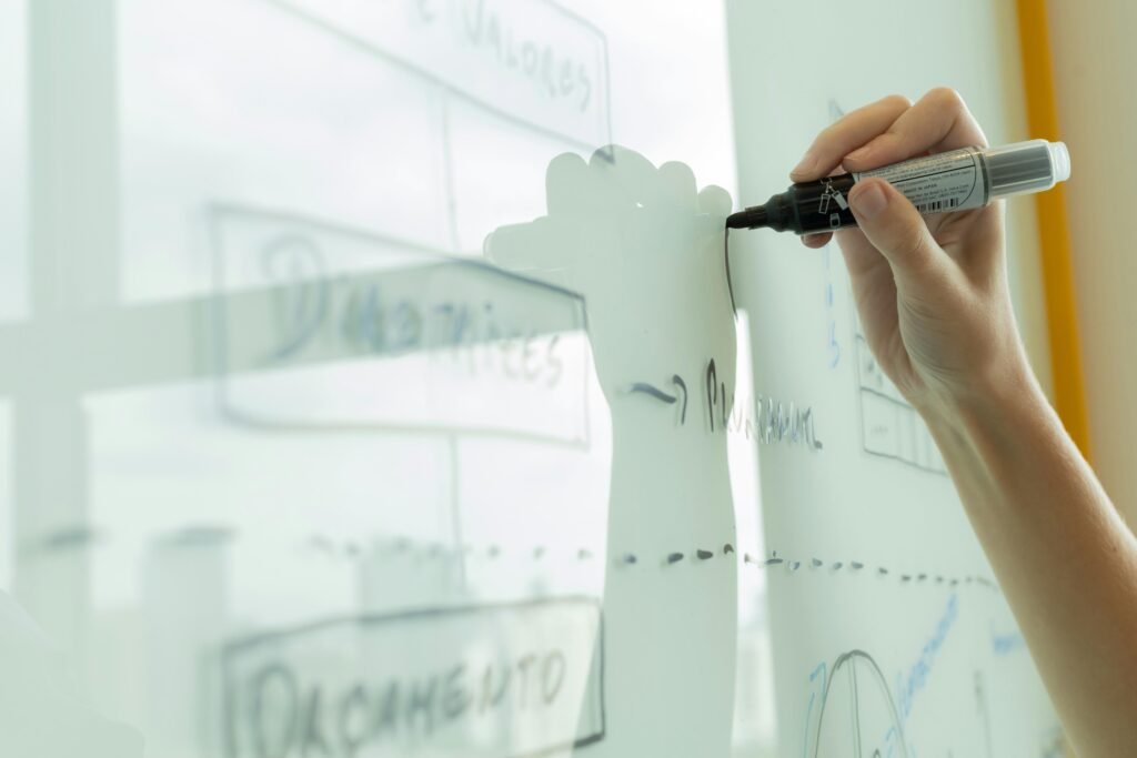 Hand zeichnet ein Diagramm auf ein Whiteboard, um komplexe Abläufe oder Strategien visuell zu veranschaulichen.