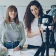 Zwei Frauen filmen gemeinsam ein Video zum Thema Mode mit professioneller Ausrüstung in einem modernen Raum.