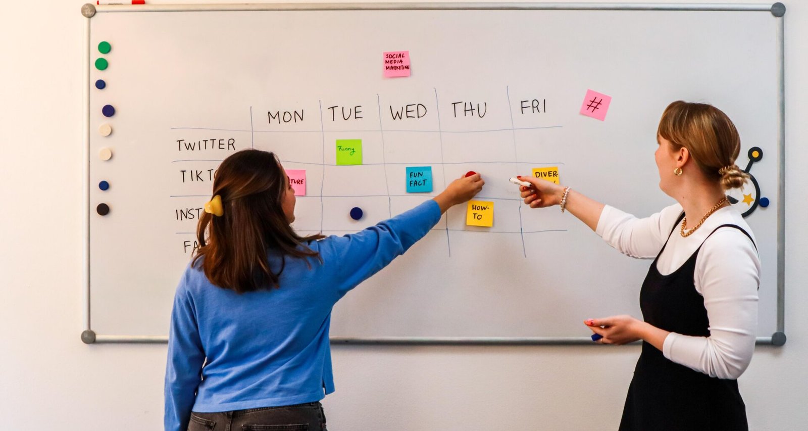 Zwei Frauen schreiben an einem Whiteboard mit vielen bunten Klebezetteln während einer Teambesprechung.