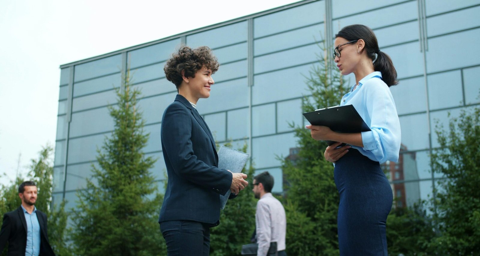 Zwei Geschäftsfrauen im Gespräch vor einem modernen Bürogebäude im Freien, Fokus auf Networking und Austausch.