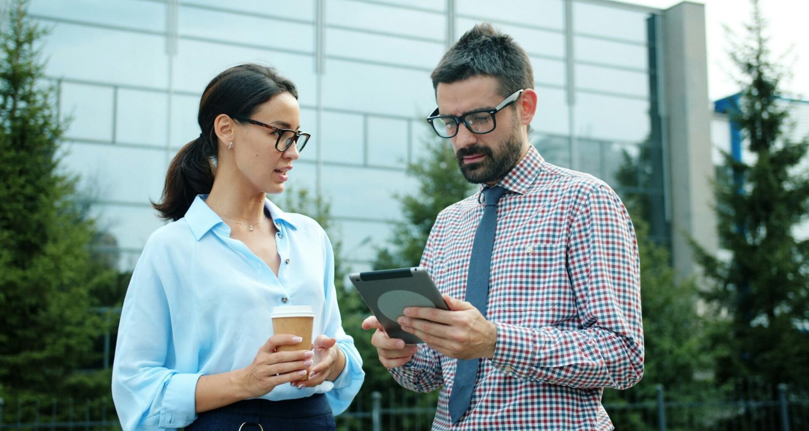 Zwei Geschäftspersonen stehen draußen und schauen gemeinsam auf ein Tablet, nutzen digitale Technik im Arbeitsalltag.