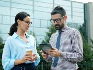 Zwei Geschäftspersonen stehen draußen und schauen gemeinsam auf ein Tablet, nutzen digitale Technik im Arbeitsalltag.