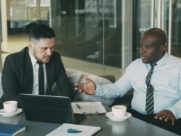 Zwei Geschäftsmänner sitzen gemeinsam an einem Tisch und besprechen ein Projekt in moderner Arbeitsumgebung.