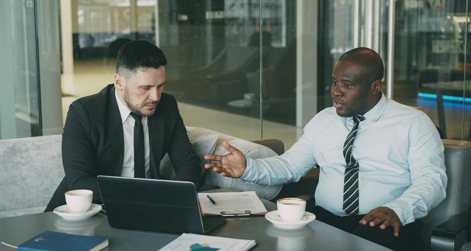 Zwei Geschäftsmänner sitzen an einem Tisch und diskutieren gemeinsam über ein Projekt in einem modernen Büro.