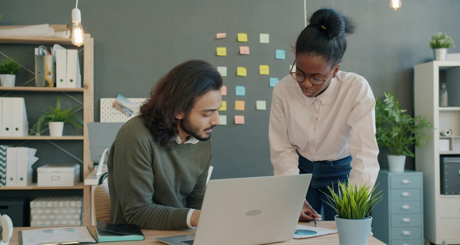 Zwei Kollegen sitzen an einem Schreibtisch und besprechen gemeinsam ein Projekt mit Laptop und Unterlagen im Büro.