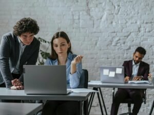 Zwei Kollegen sitzen in einem Büro und arbeiten gemeinsam an einem offenen Laptop auf einem Schreibtisch.