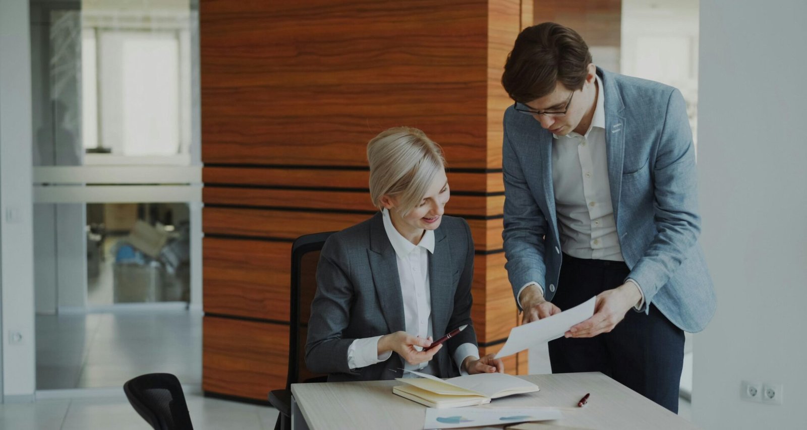 Zwei Kollegen sitzen an einem Schreibtisch im Büro und diskutieren geschäftliche Unterlagen miteinander