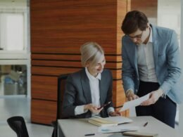 Zwei Kollegen sitzen an einem Schreibtisch im Büro und diskutieren geschäftliche Unterlagen miteinander