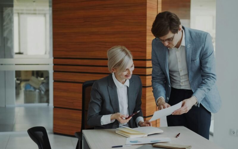 Zwei Kollegen sitzen an einem Schreibtisch im Büro und diskutieren geschäftliche Unterlagen miteinander