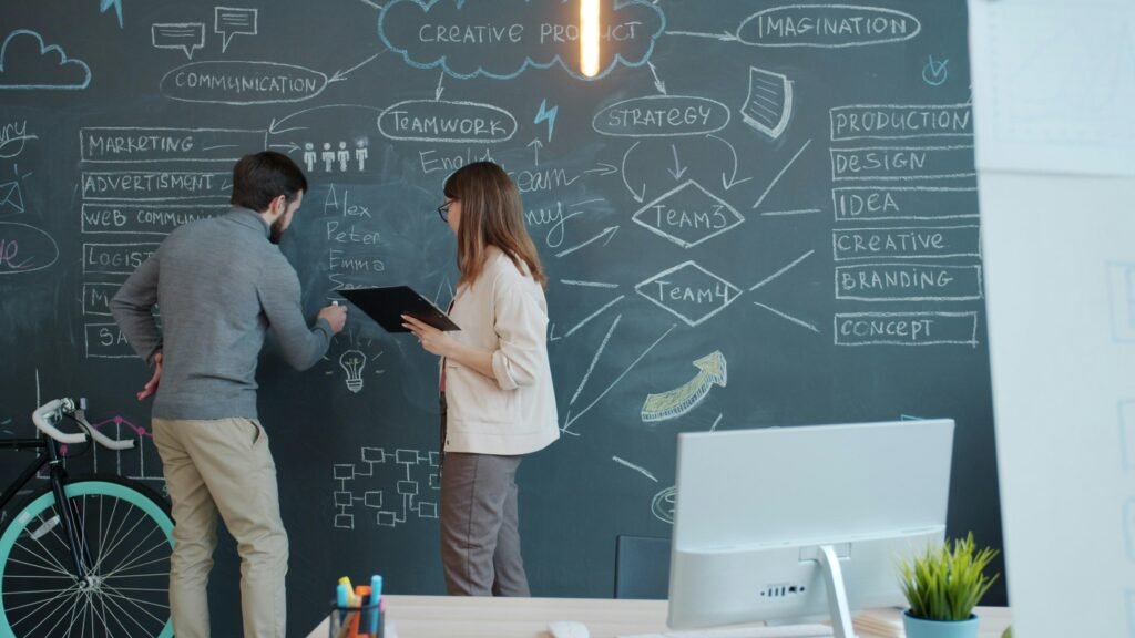 Zwei Menschen stehen vor einer großen Tafelwand und skizzieren verschiedene Ideen mit Kreide während eines Brainstormings.
