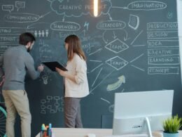 Zwei Menschen stehen vor einer großen Tafelwand und skizzieren verschiedene Ideen mit Kreide während eines Brainstormings.