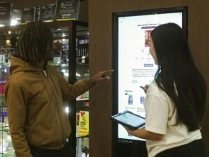 Zwei Menschen stehen vor einem großen digitalen Display und bedienen die interaktive Benutzeroberfläche.