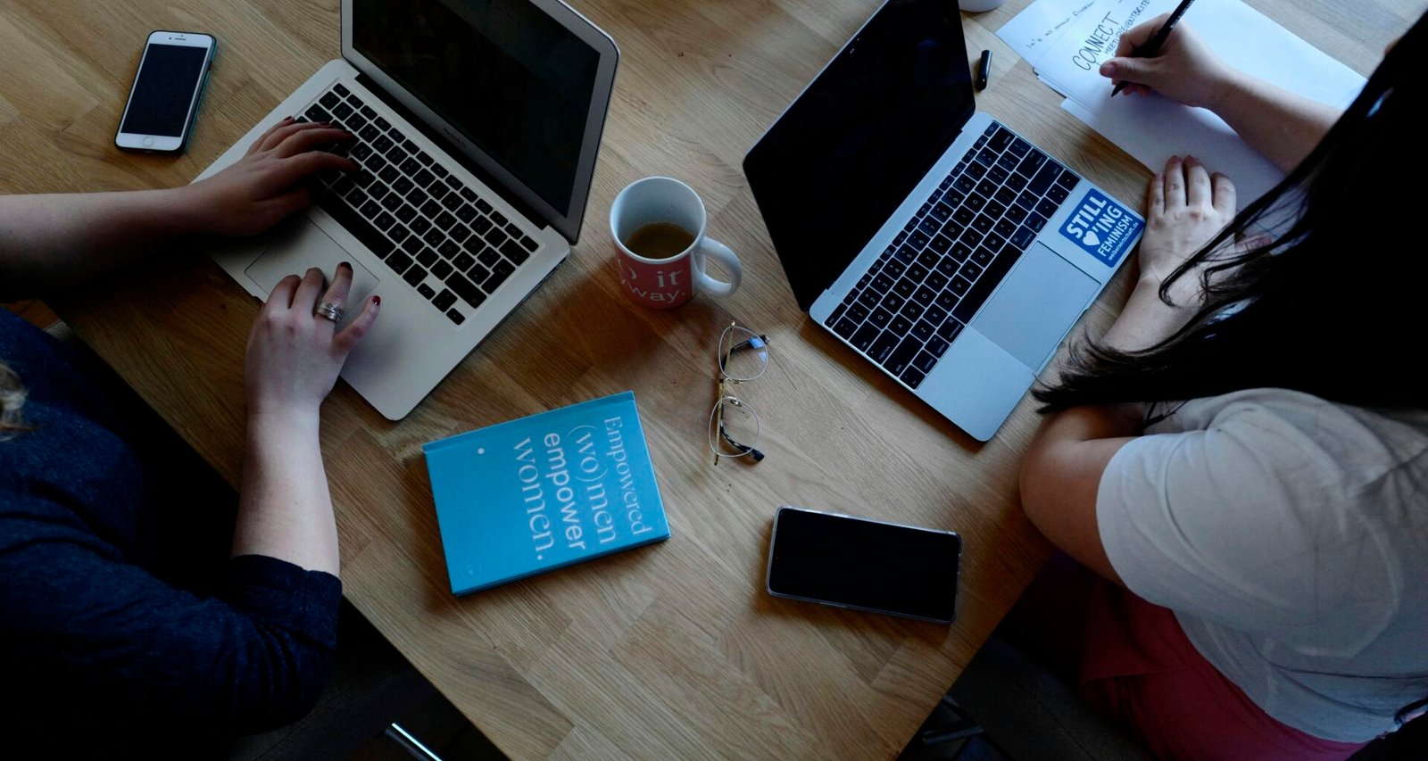 Zwei Personen sitzen an einem Tisch und arbeiten konzentriert an ihren Laptops in einem modernen Arbeitsumfeld.