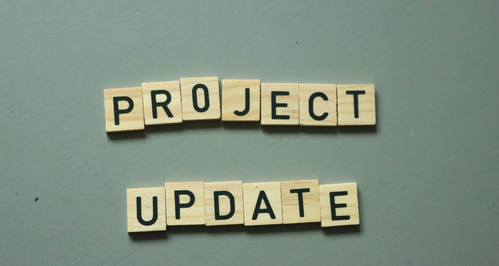Zwei Scrabble-Steine mit den Worten project update liegen nebeneinander auf einem Holztisch und symbolisieren eine Projektaktualisierung.