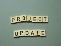 Zwei Scrabble-Steine mit den Worten project update liegen nebeneinander auf einem Holztisch und symbolisieren eine Projektaktualisierung.