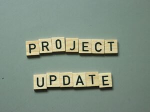 Zwei Scrabble-Steine mit den Worten project update liegen nebeneinander auf einem Holztisch und symbolisieren eine Projektaktualisierung.