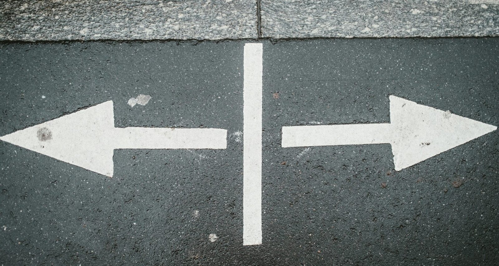 Zwei weiße Pfeile, die auf dunkelgrauem Asphalt in entgegengesetzte Richtungen zeigen, fotografiert von oben